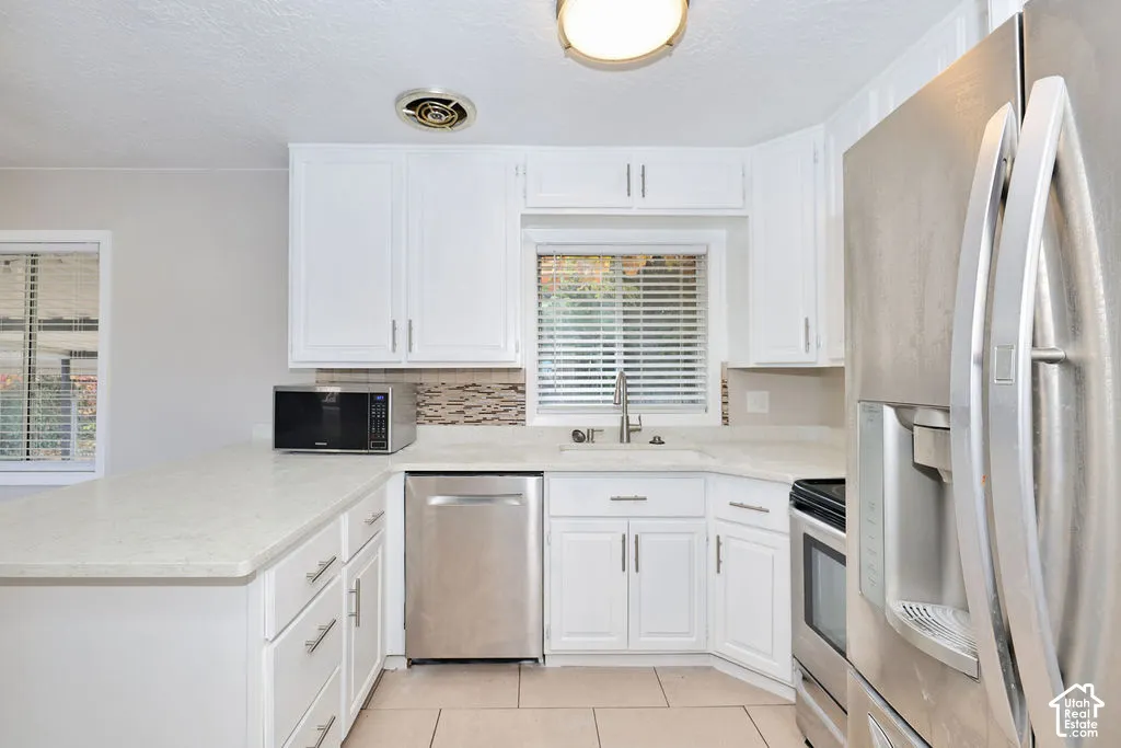 Kitchen featuring white cabinetry, stainless steel appliances, neutral countertops, stone-finish backsplash, and tile flooring