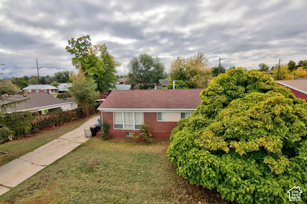 Single-level brick exterior with a pitched shingle roof, concrete driveway, and established landscape