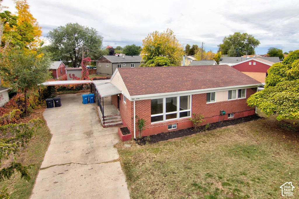 Single-story brick exterior featuring a shingle roof, large multi-pane windows, a concrete driveway, and an attached carport