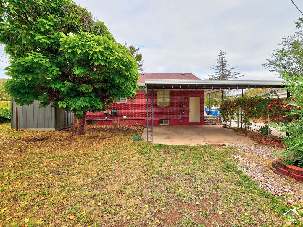 Red brick exterior featuring a metal-roofed carport, concrete pad, detached metal storage structure, and mature landscaping