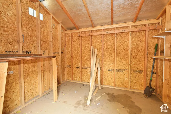 Storage structure featuring exposed wood-stud framing, oriented strand board wall panels, a concrete floor, and integrated wall-mounted shelving
