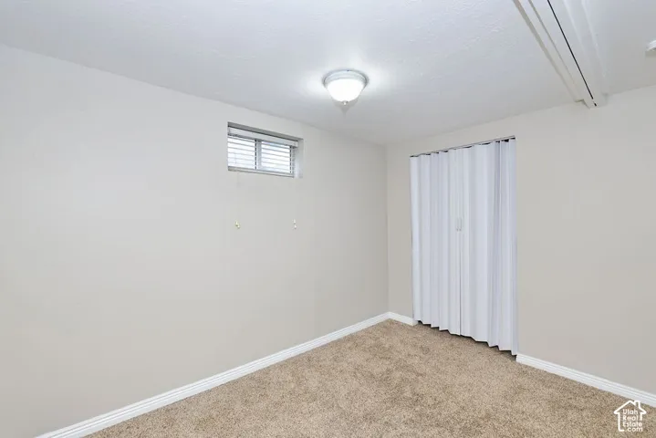 Neutral-toned room featuring neutral carpeting, a built-in accordion-style closet door, and an exterior window with a horizontal blind