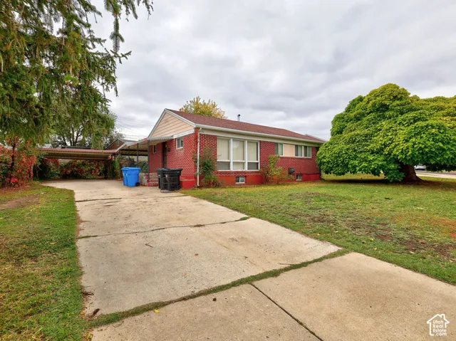Single-story residence with red brick exterior, concrete driveway, attached carport, and mature trees