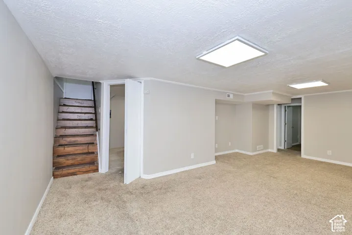 Open-concept room featuring neutral-toned carpeting, square recessed ceiling lighting, and wooden stair treads