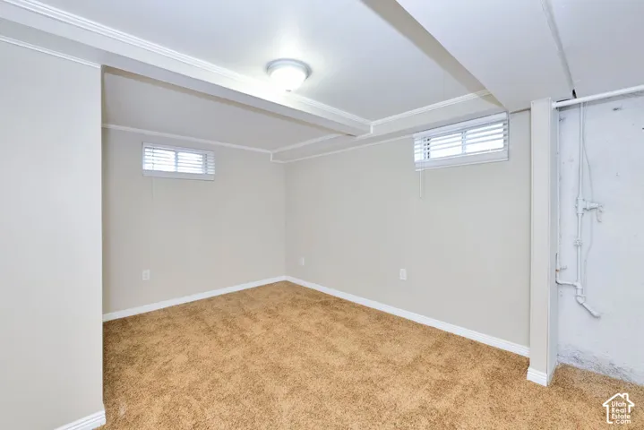 Carpeted interior featuring neutral-toned walls, structural ceiling beams, two rectangular windows with horizontal blinds, and a flush-mount ceiling fixture