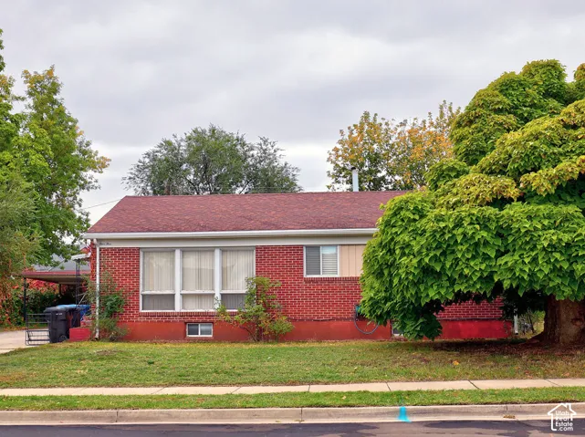Single-story red brick exterior featuring a shingled roof, large multi-pane windows, and a side-mounted carport