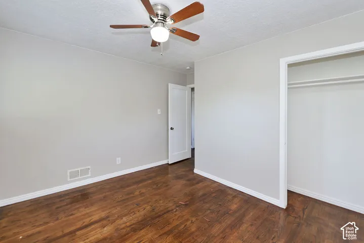 Room featuring wood-finish flooring, a ceiling fan with integrated lighting, neutral wall paint, and a built-in closet with shelving