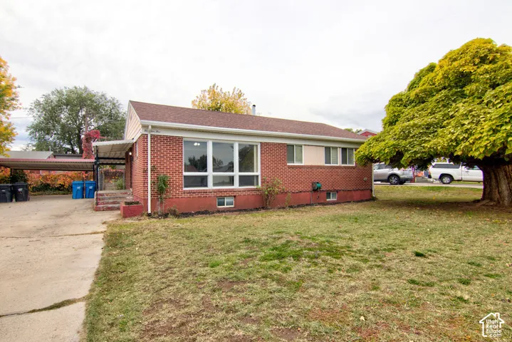Red brick exterior featuring a multi-pane picture window, asphalt shingle roof, concrete driveway, and covered carport