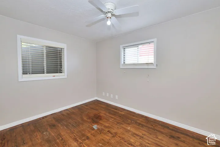 Wood-finish flooring, neutral wall tones, two dual-pane windows, and a central ceiling fan with an integrated light fixture