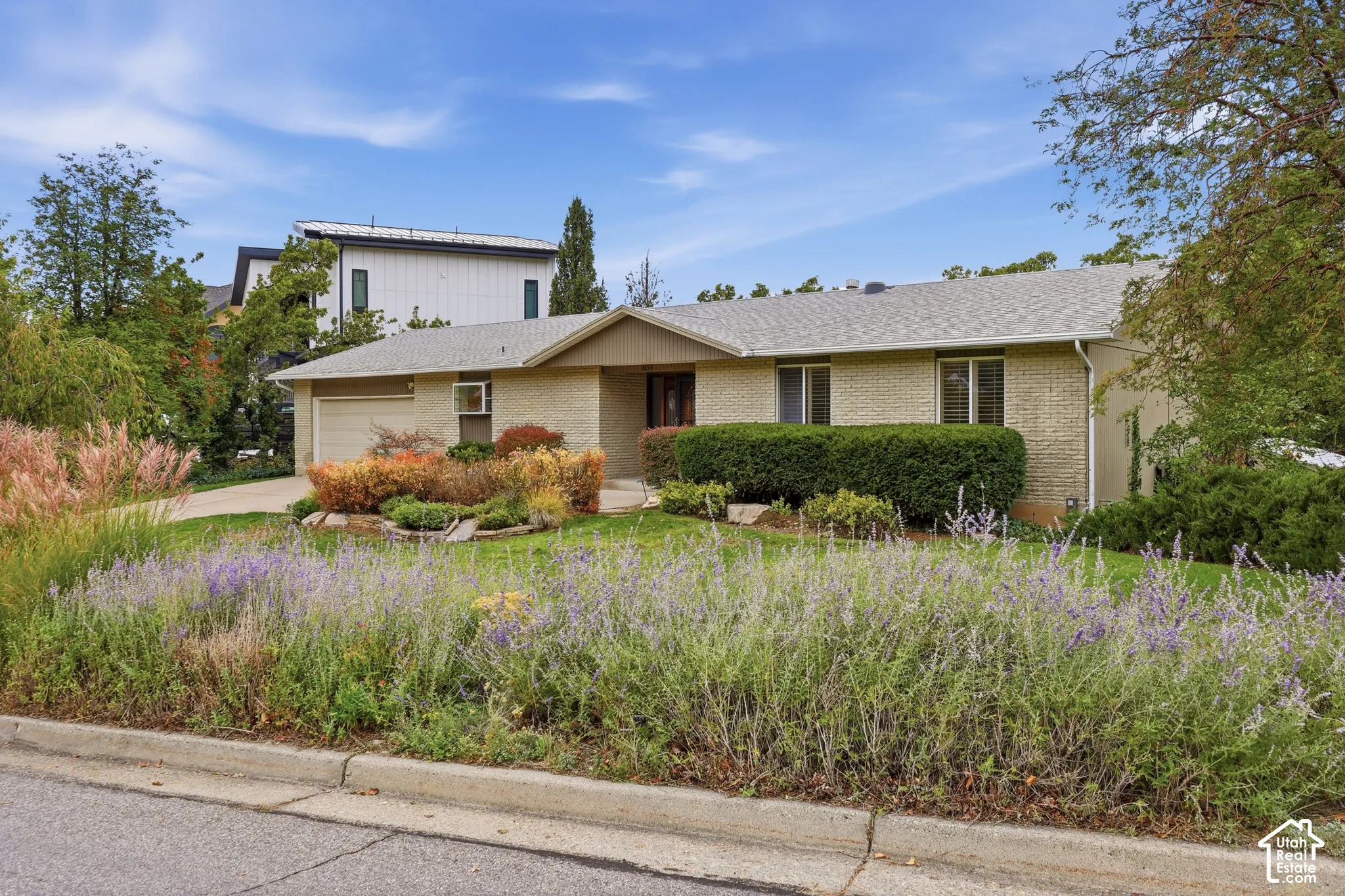 Single-story brick exterior featuring a low-slope roof, an attached garage, and mature landscaping