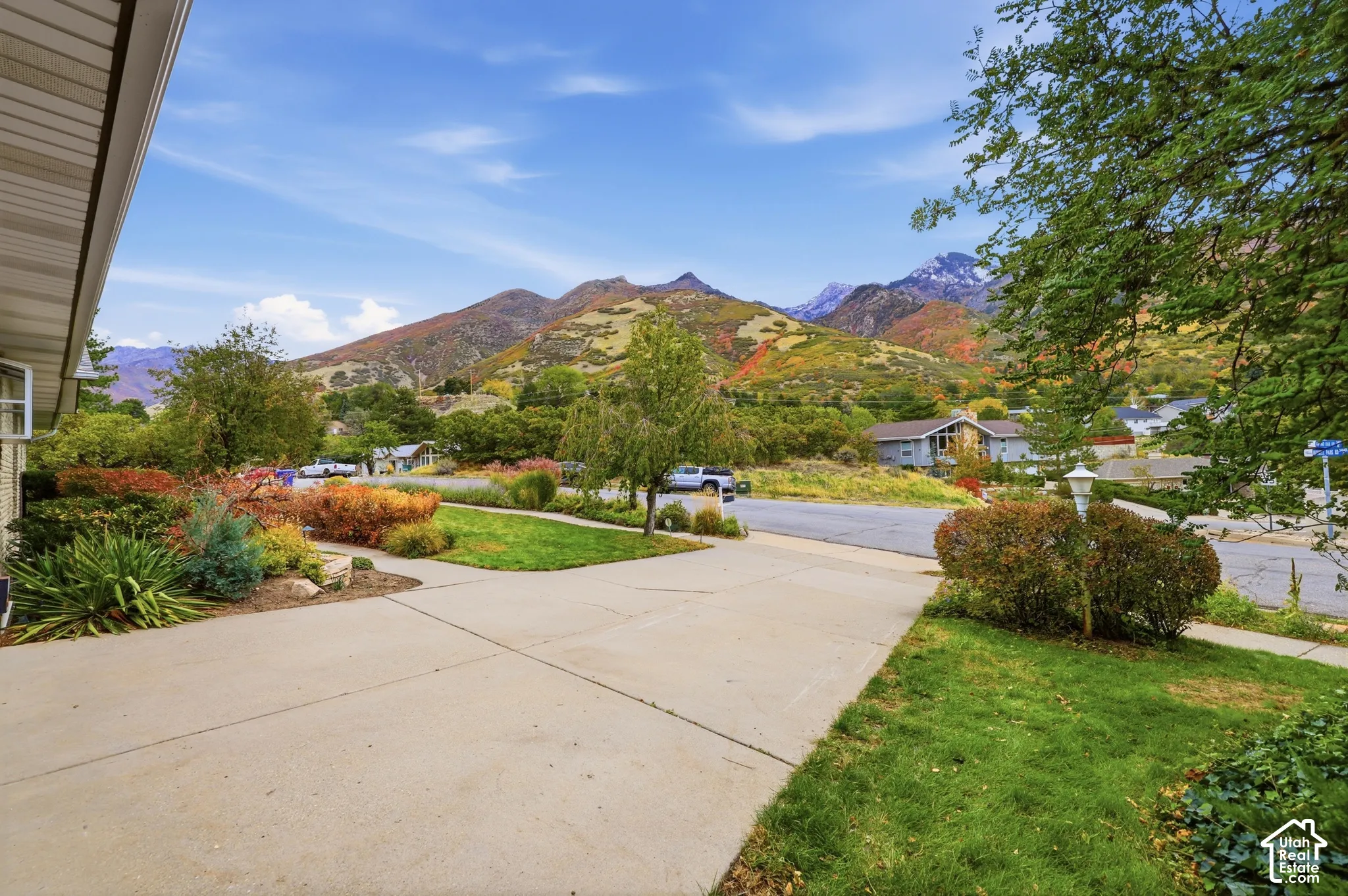 Concrete driveway, landscaped lawn with mature trees and shrubs, and prominent mountain backdrop.