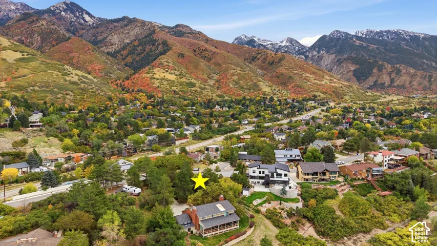 Aerial perspective featuring a multi-story residence with a pitched roof, brick chimney, and covered porch, situated on a lot with mature trees and a mountain backdrop