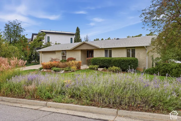 Single-story brick exterior featuring a low-slope roof, an attached garage, and mature landscaping