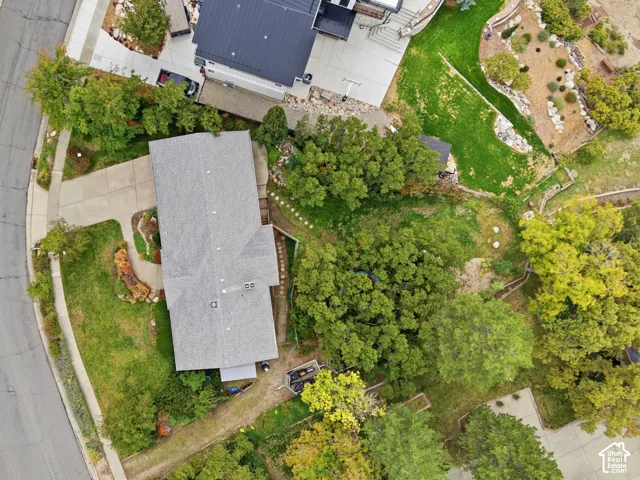 Aerial perspective featuring a pie shaped lot with a concrete driveway, multi-level landscaping, mature trees, and asphalt shingle roofing.