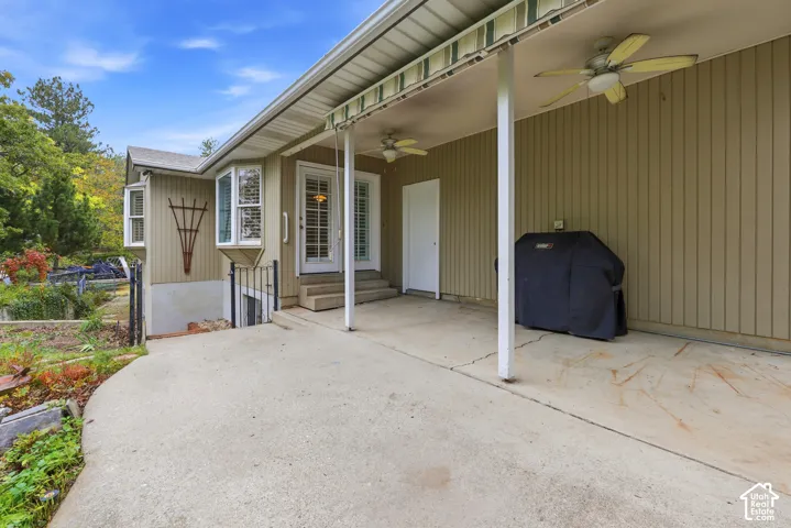 Covered concrete patio featuring vertical siding, ceiling-mounted fans, a retractable awning, and bay windows.