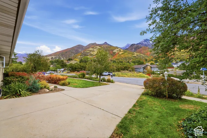 Concrete driveway, landscaped lawn with mature trees and shrubs, and prominent mountain backdrop.