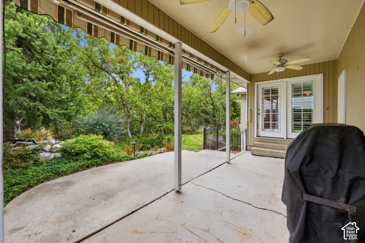 Covered concrete patio featuring a retractable fabric awning, dual ceiling fans, and access via French-style doors. Color correction applied.