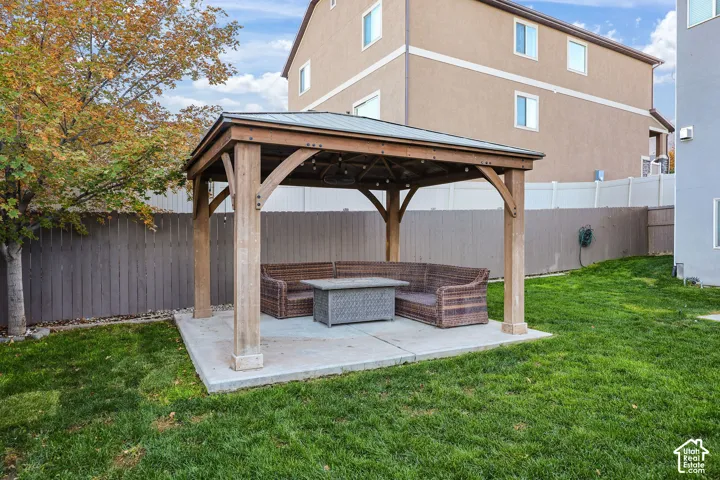 Outdoor living area featuring a covered timber-frame gazebo situated on a concrete slab, enclosed by a privacy fence and situated within a landscaped lawn