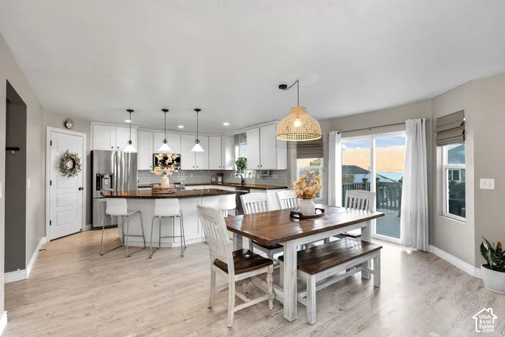 Open kitchen featuring white cabinetry, a center island with countertop seating, stainless steel appliances, wood-finish flooring, and a sliding glass door