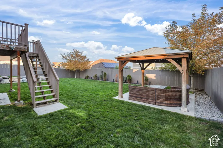 Fenced backyard featuring a manicured lawn, a detached wooden gazebo with a metal roof, an elevated wooden deck with stairs, and stone ground cover