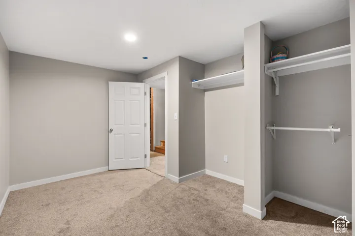 Neutral-toned room with wall-to-wall carpeting, recessed ceiling lighting, a six-panel door, and built-in closet shelving with hanging rods