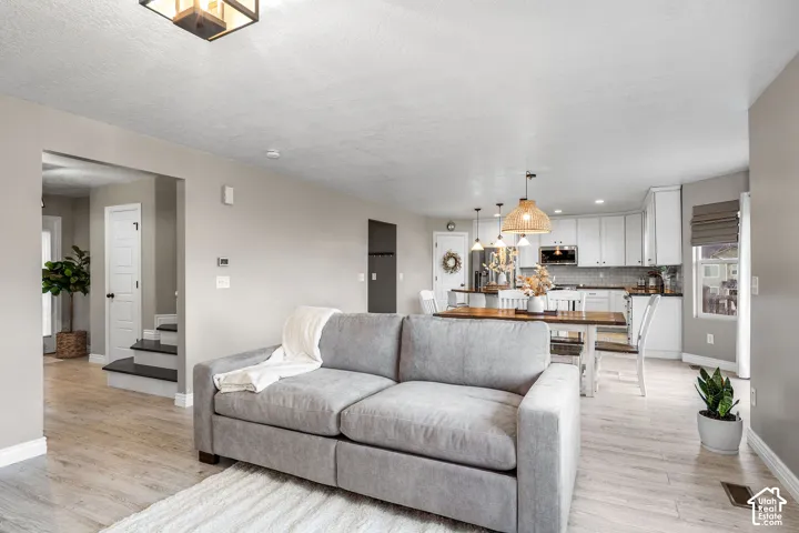 Open-concept interior featuring light wood-finish flooring, white kitchen cabinetry, a geometric ceiling light fixture, recessed lighting, and a neutral wall palette