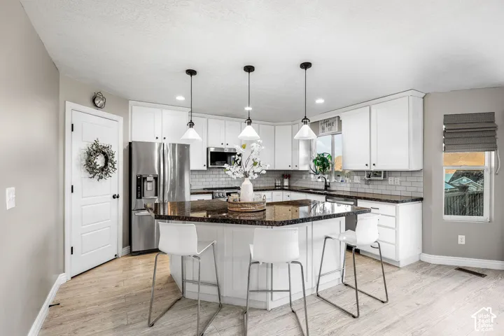 Kitchen featuring white shaker-style cabinetry, dark stone countertops, a subway tile backsplash, stainless steel appliances, and wood-finish flooring