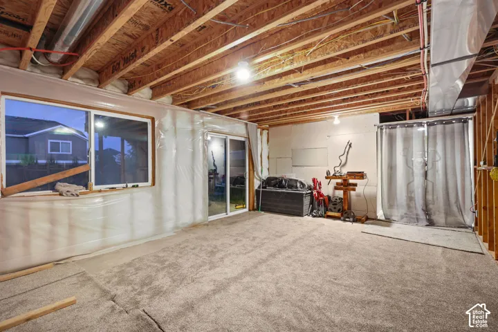Unfinished space featuring exposed wood-joist ceiling, carpeted flooring, large sliding glass door, and wide window
