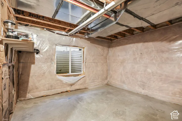 Unfinished interior space featuring exposed wood joists, concrete flooring, plastic vapor barrier wall covering, and a recessed window well