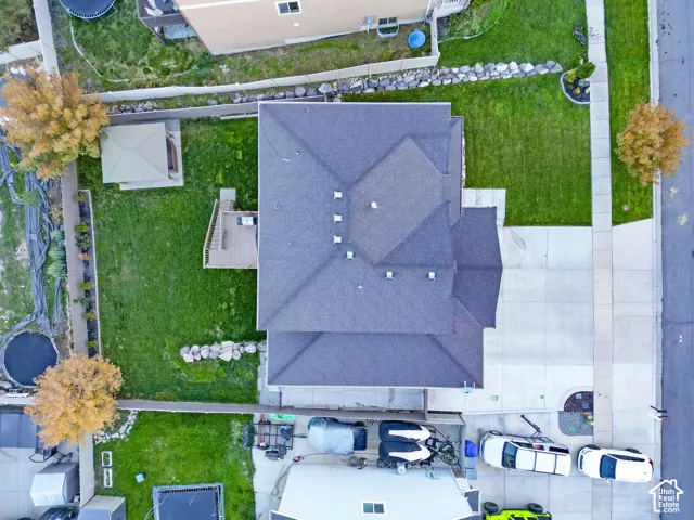 Aerial view featuring a multi-faceted shingle roof, concrete driveway, fenced yard, and a deck