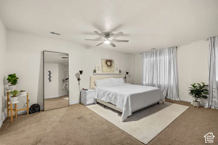 Neutral-toned room featuring wall-to-wall carpeting, a ceiling-mounted light fixture with fan, and wall-mounted sconces