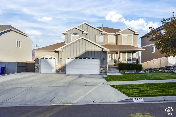 Multi-level exterior featuring vertical siding, stone masonry accents, a three-car garage, and a manicured lawn