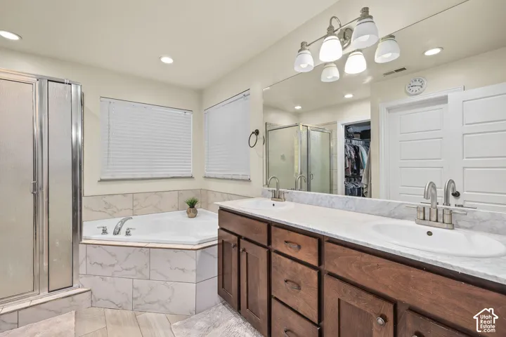 Dual-sink vanity with stone-finish countertop, corner soaking tub with tile surround, glass-enclosed shower, and full-width vanity mirror
