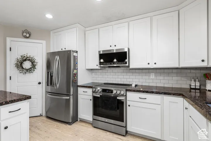 Kitchen featuring white cabinetry, dark stone countertops, stainless steel appliances, and a subway tile backsplash
