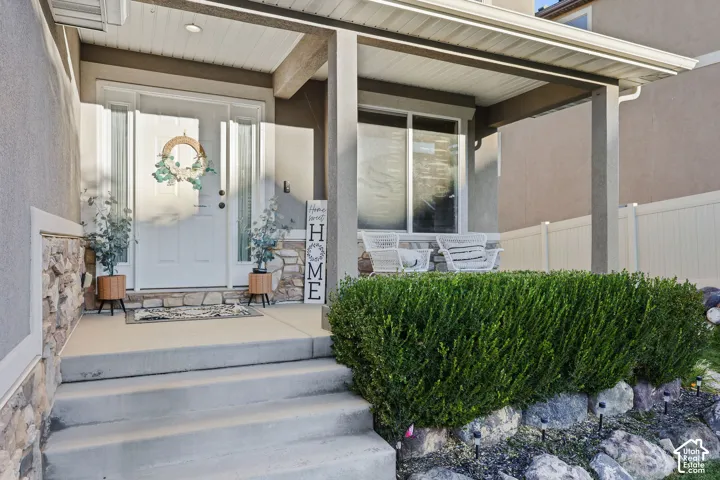 Covered front porch featuring concrete steps, stacked stone accents, and a panelled front door with sidelights