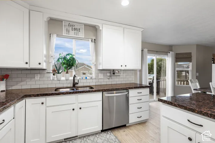 Kitchen featuring white Shaker-style cabinetry, dark stone-finish countertops, subway tile backsplash, stainless steel dishwasher, and wood-finish flooring