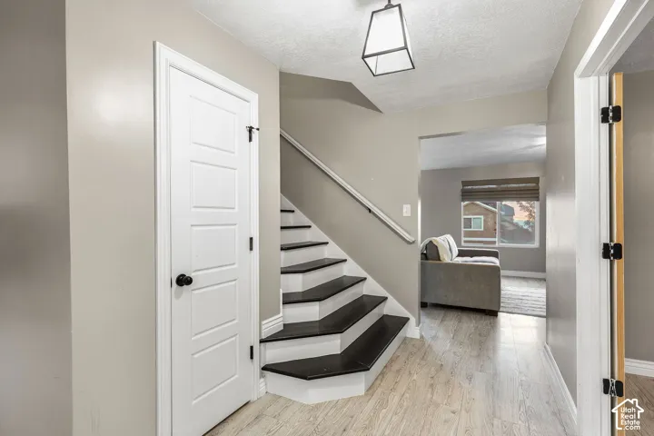 Staircase featuring wood-finish treads and white risers with a metal handrail, wood-finish flooring, paneled interior door with matte black hardware, and geometric pendant lighting