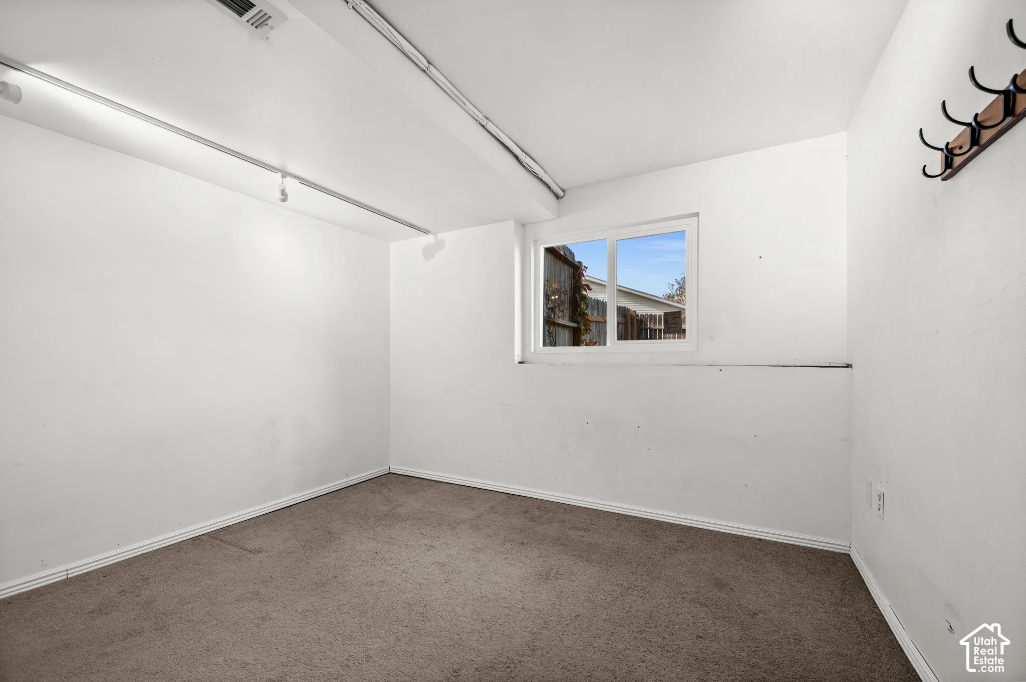 Neutral-toned carpet, white walls, sliding window, and a wall-mounted hook rail