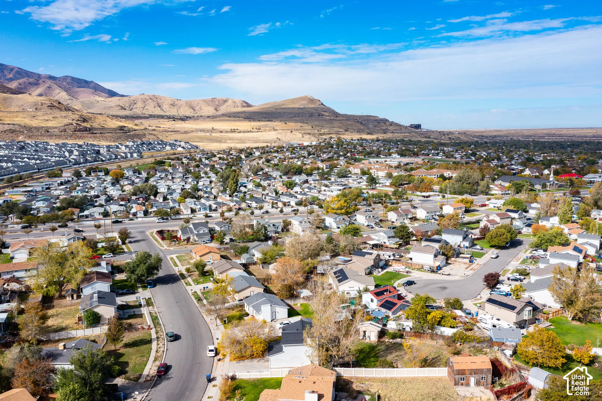 Aerial perspective of a residential neighborhood featuring paved streets, mature trees, and mountainous topography in the distance