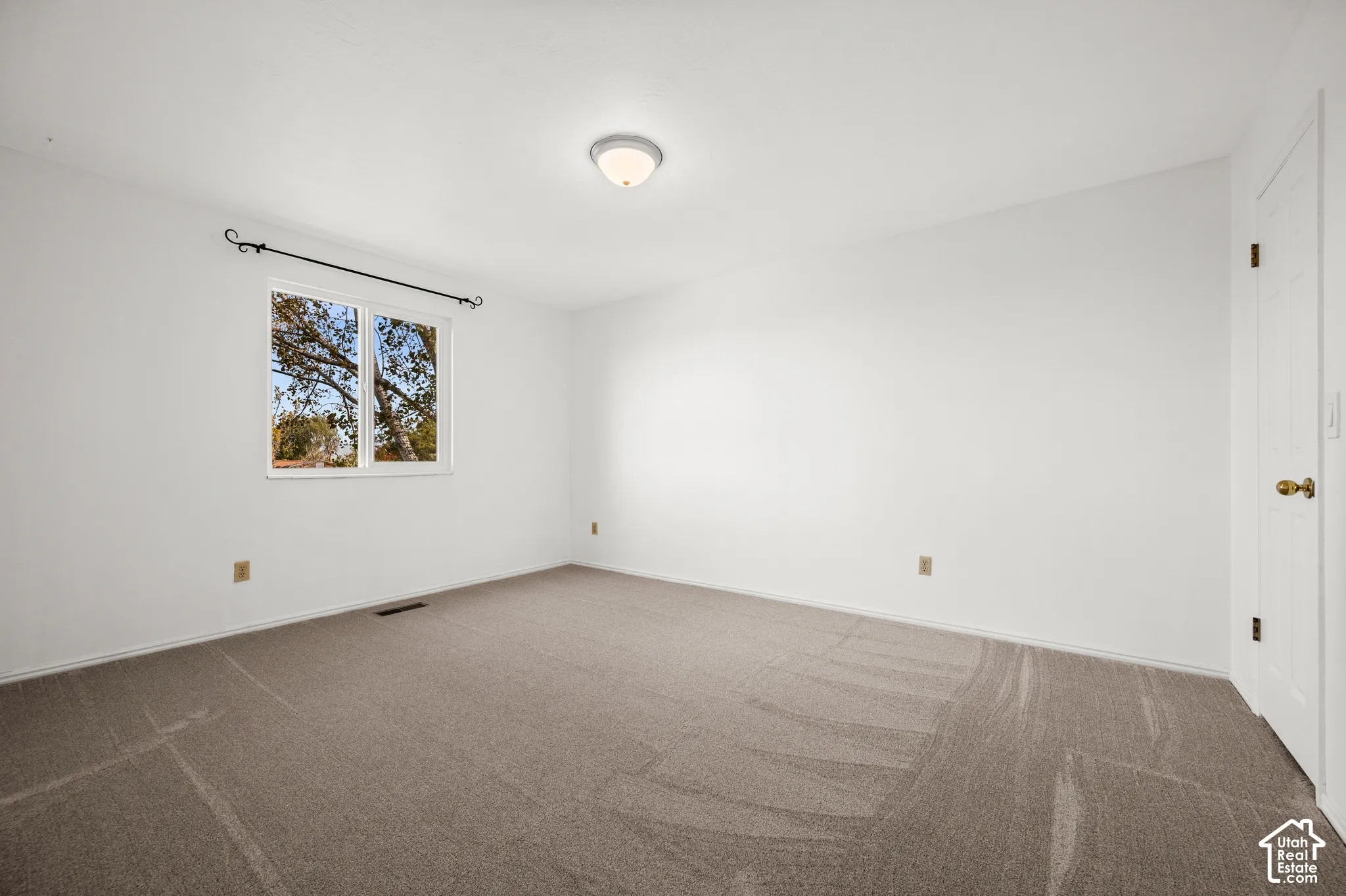 Neutral-toned carpeting, crisp white walls, flush-mount dome lighting, and a single-pane window with hardware