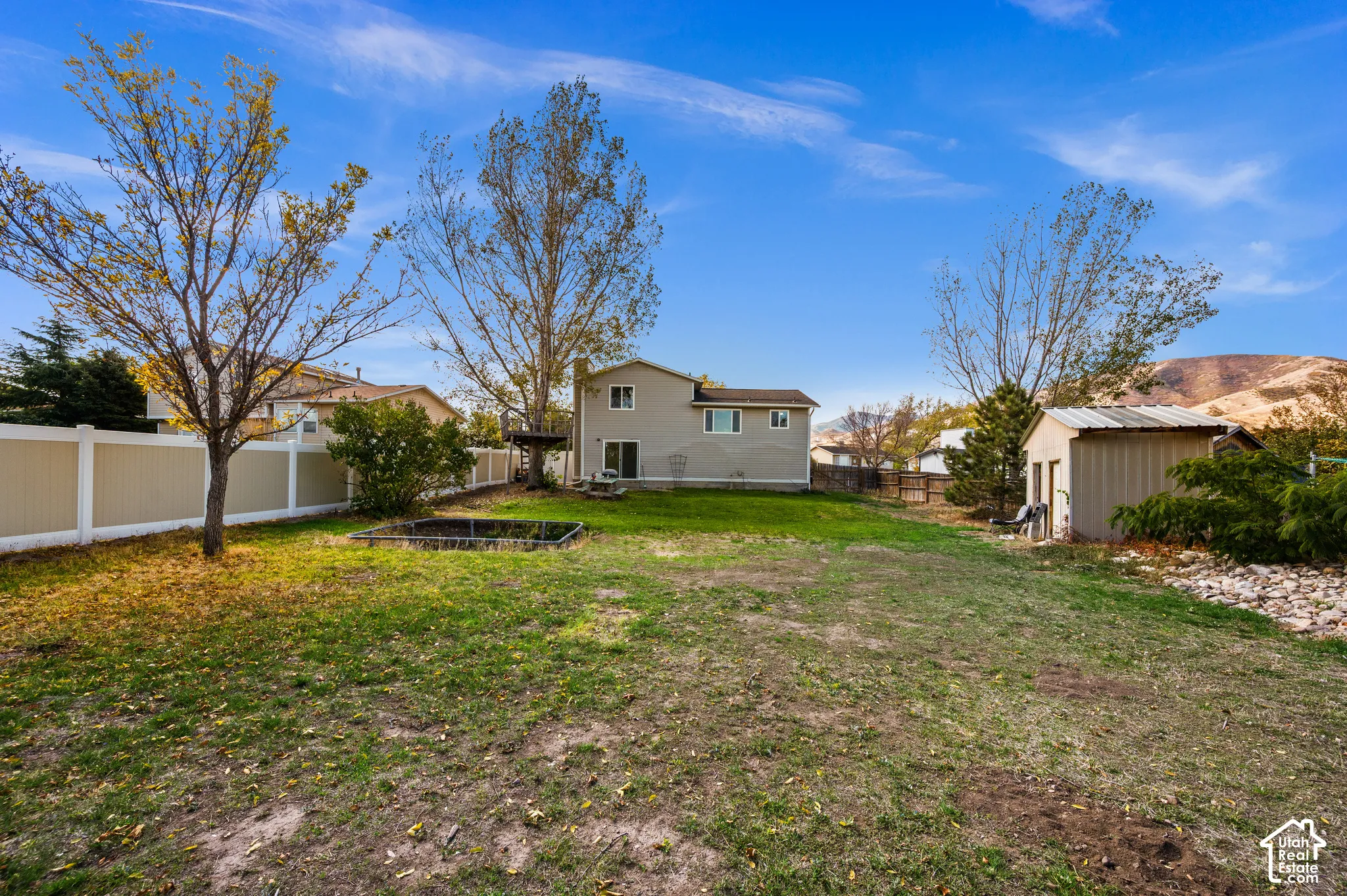 Expansive backyard featuring a tall privacy fence, mature trees, a detached storage shed, and mountain backdrop