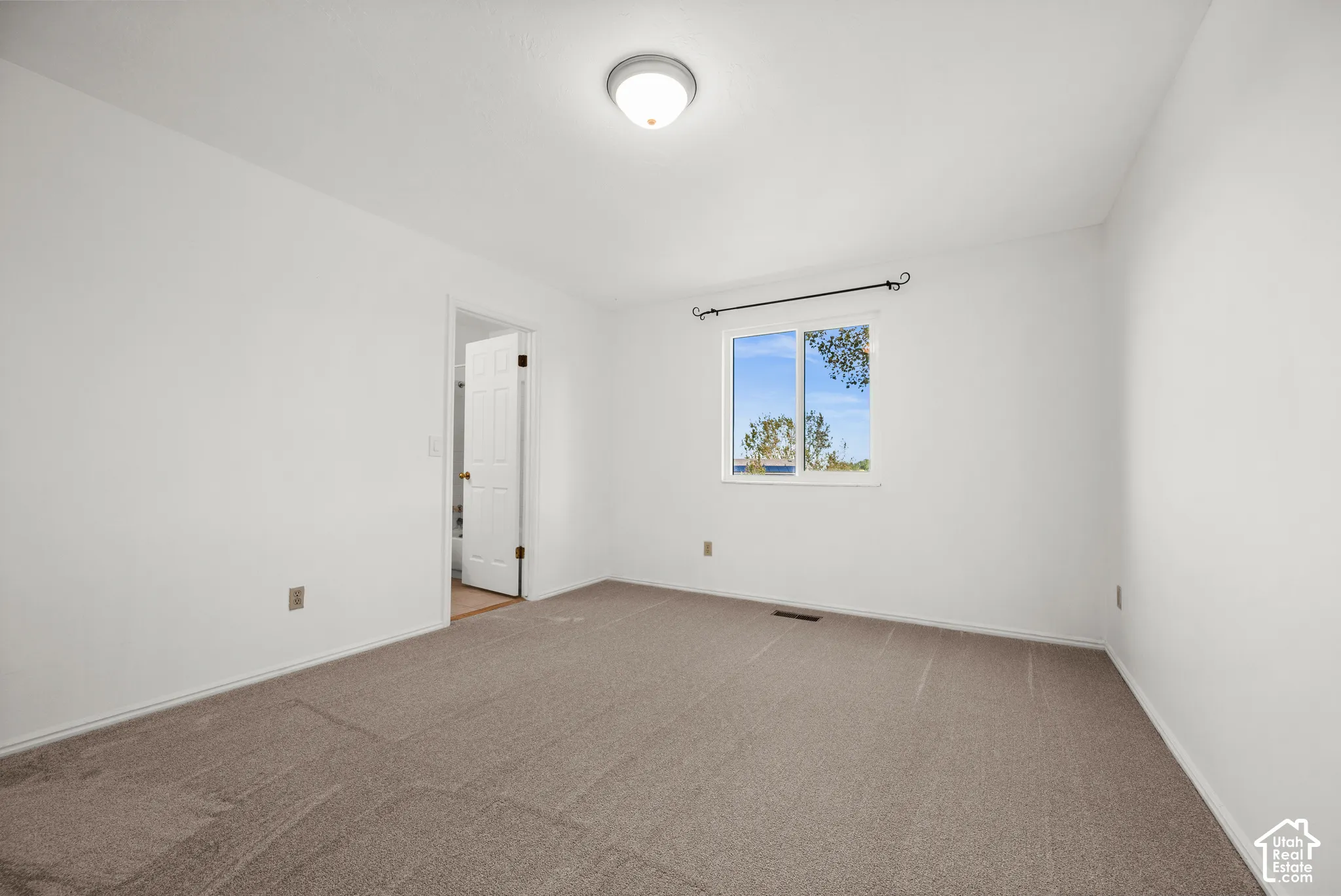 Neutral-toned carpeting, single-pane slider window with rod hardware, and flush-mount ceiling light fixture