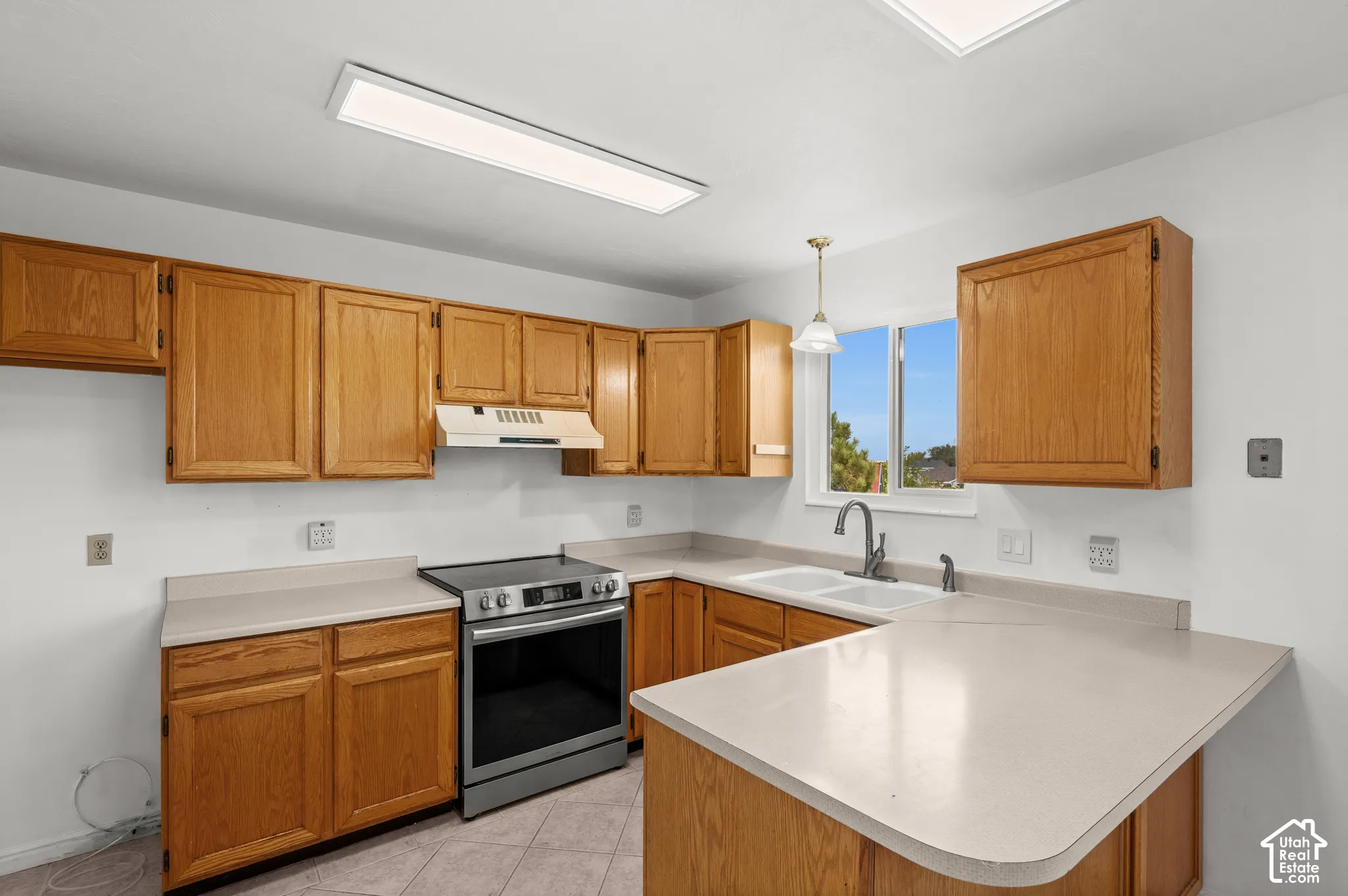 Kitchen featuring medium-tone wood cabinetry, solid-surface countertops, dual-basin sink with a gooseneck faucet, stainless steel range, and tile flooring
