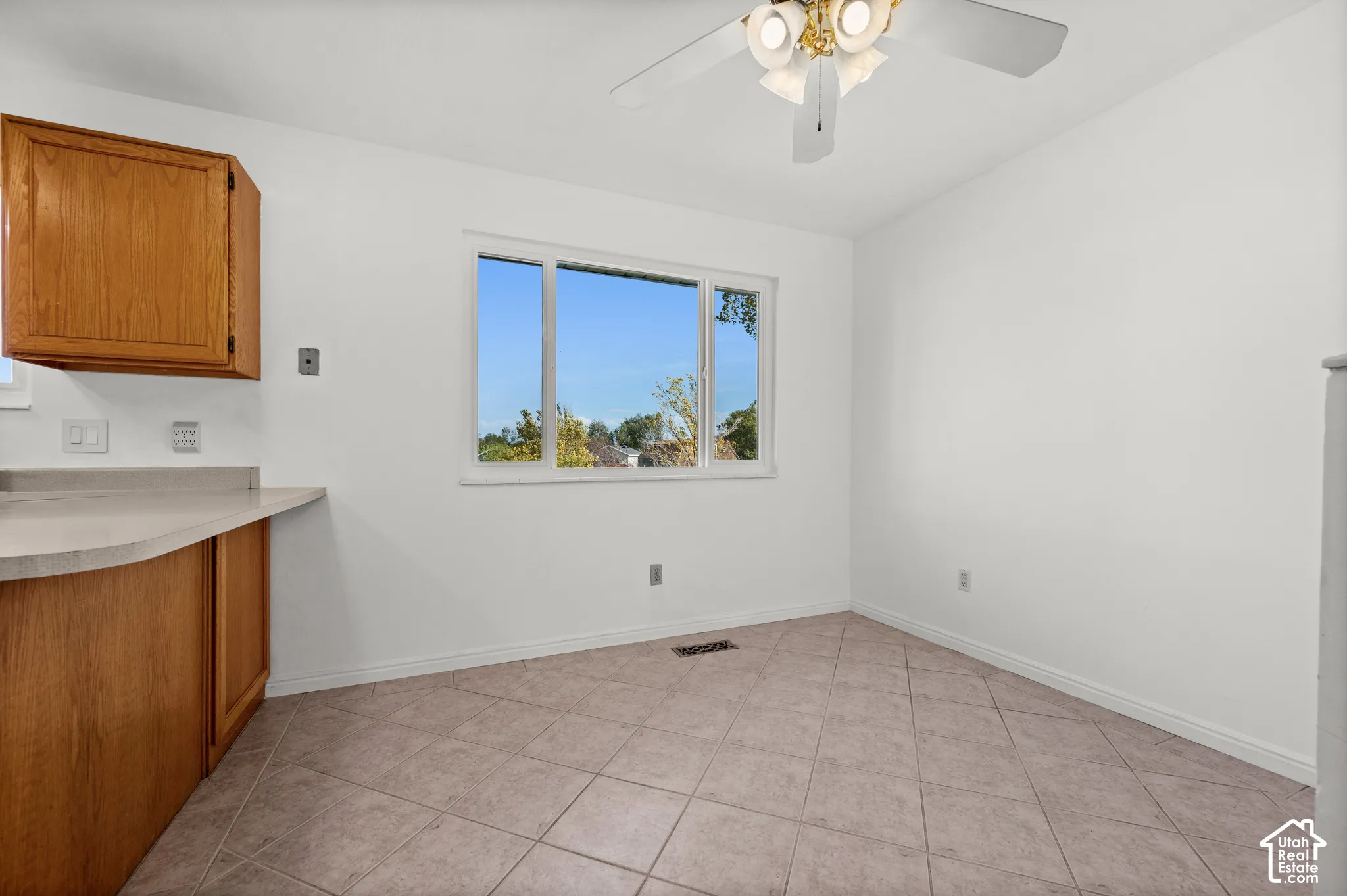 Kitchen area featuring tile flooring, wooden cabinetry, stone-finish countertops, and an overhead ceiling fan with light fixture