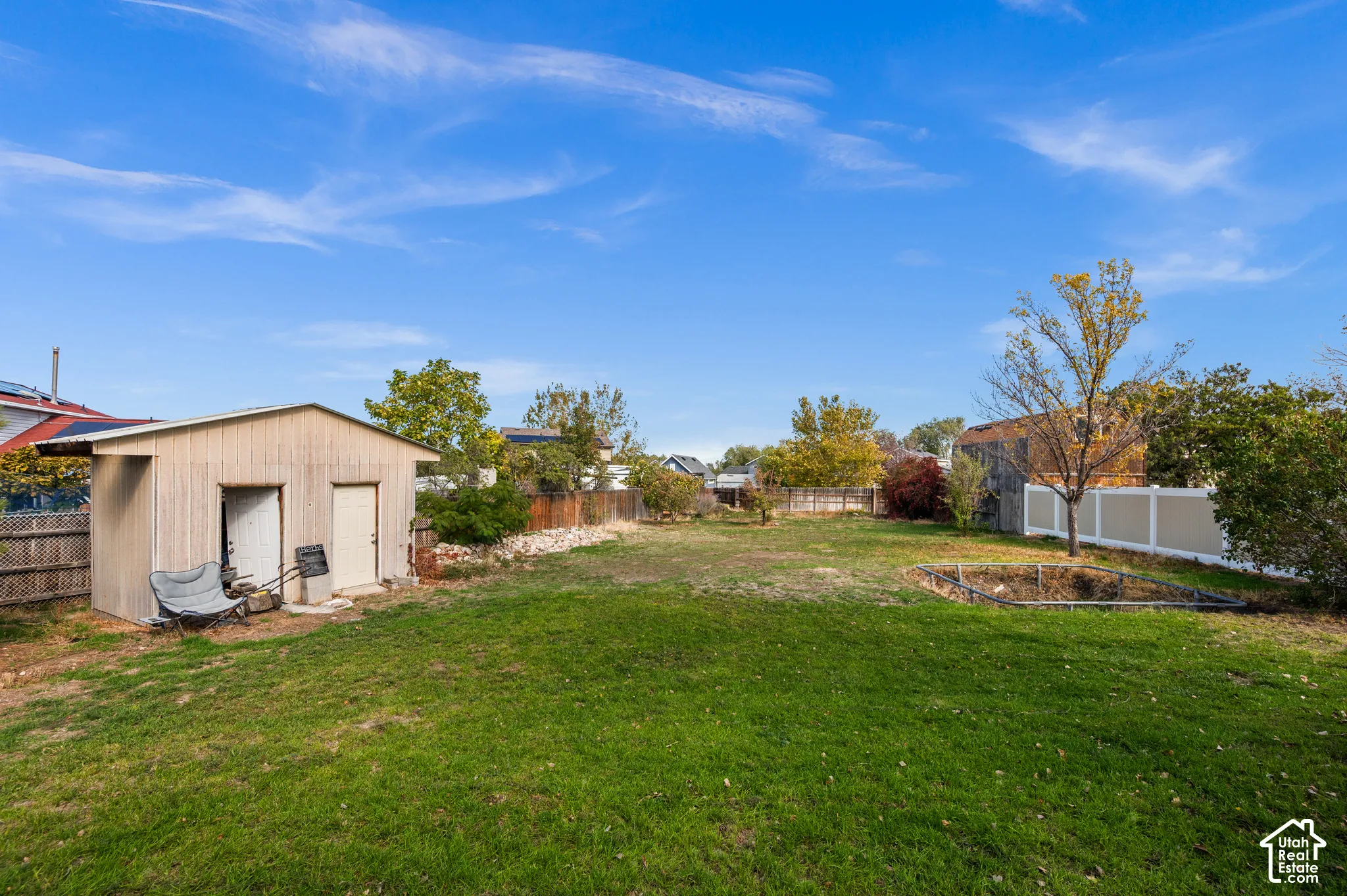 Expansive backyard featuring a grass lawn, detached storage structure, perimeter fencing, and mature trees