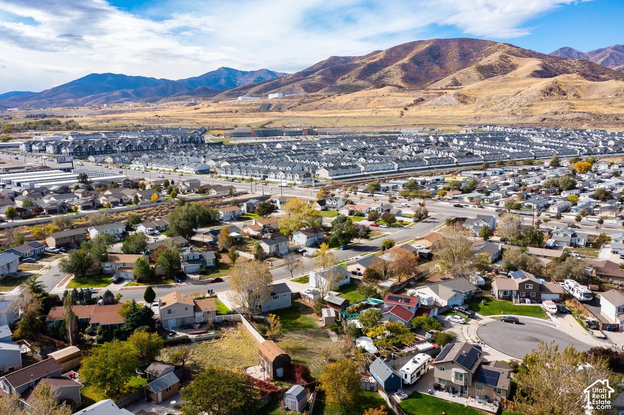 Aerial perspective of a residential neighborhood featuring established trees, paved street networks, fenced yards, and a prominent mountain range backdrop