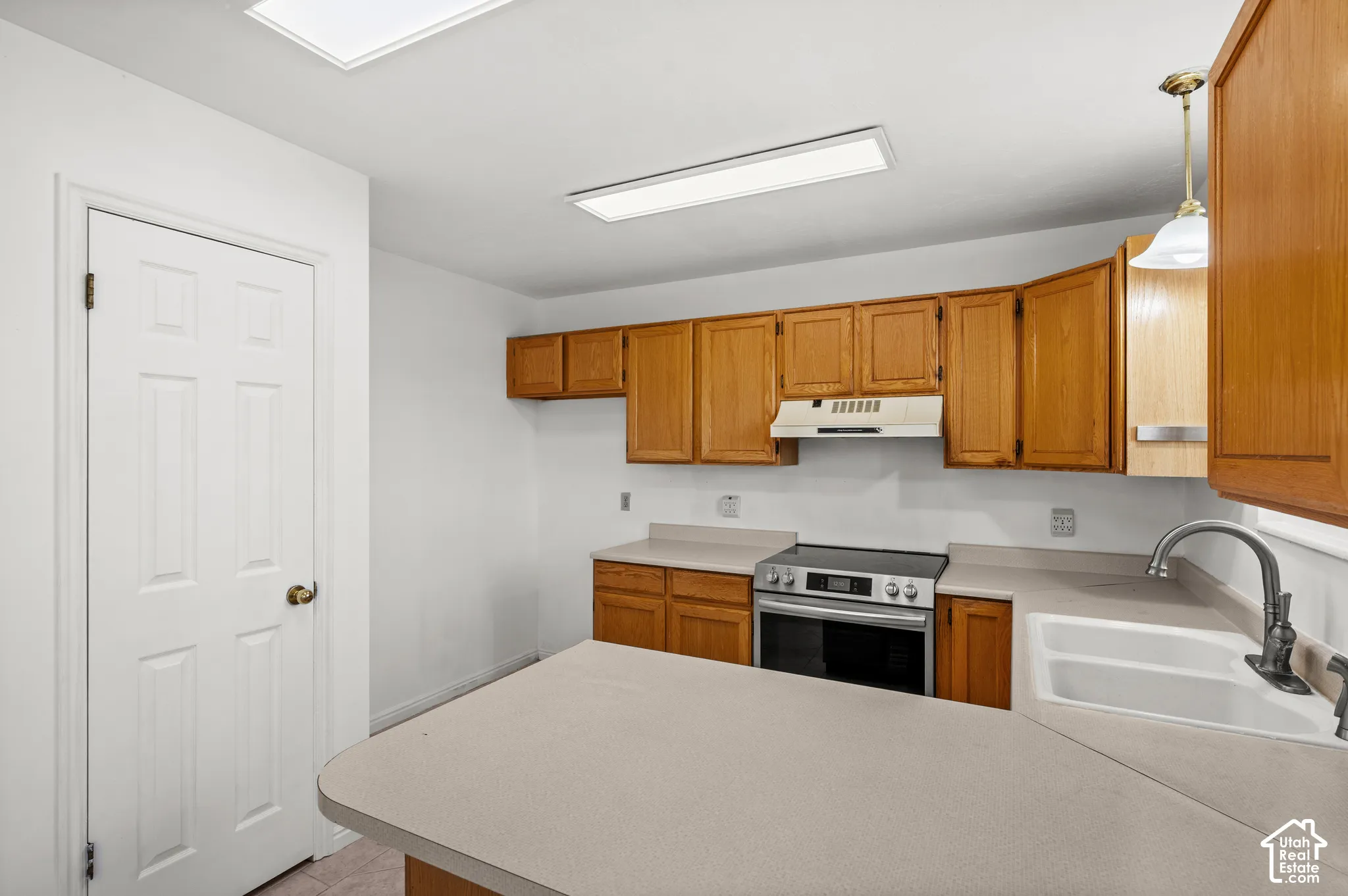 Kitchen featuring oak-finish cabinetry, neutral solid-surface countertops, dual-basin sink with a gooseneck faucet, integrated range, and recessed ceiling lighting