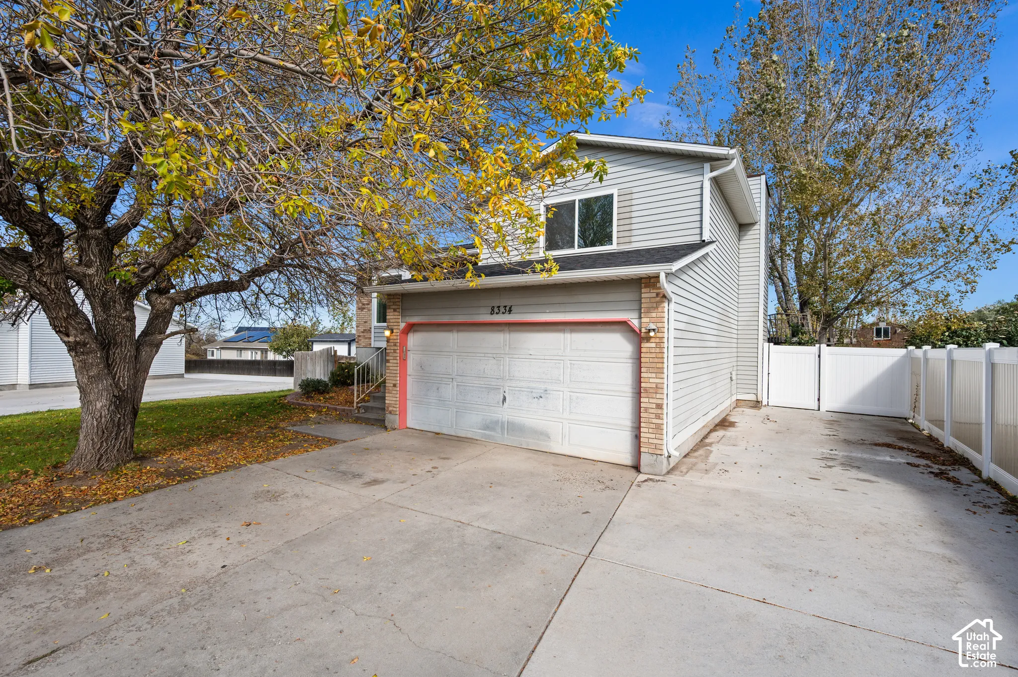 Two-story residence featuring light gray horizontal siding, an attached garage, concrete driveway, and white vinyl privacy fencing