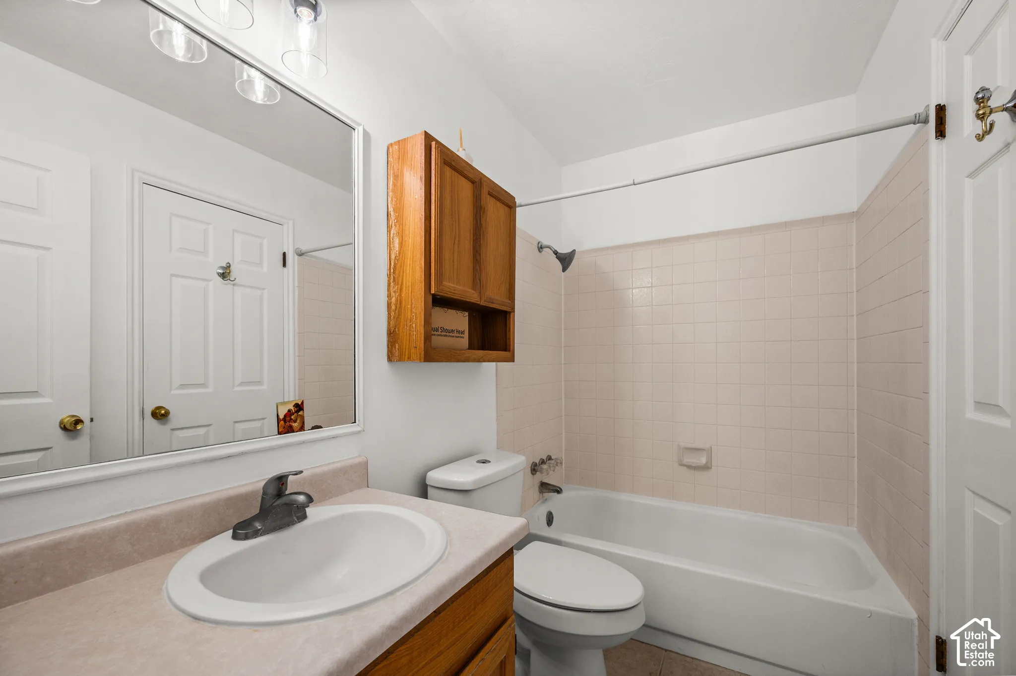 Bathroom featuring a wood-finish vanity with a molded countertop, integrated sink, wall-mounted cabinetry, a large vanity mirror with overhead lighting, and a bathtub with tile surround