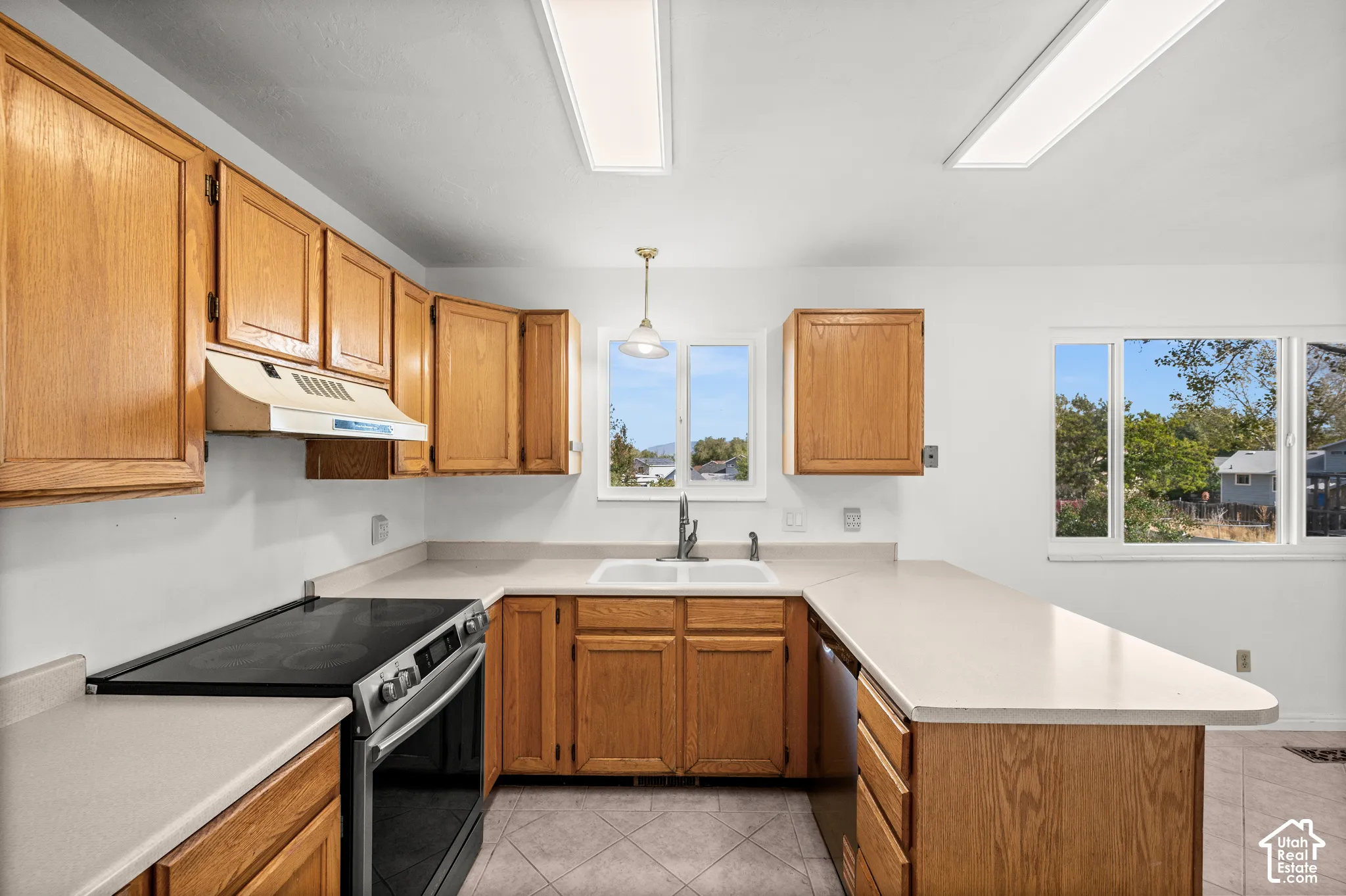 Kitchen featuring wood cabinetry, solid-surface countertops, dual-basin sink, integrated range, and ceramic tile flooring